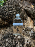 Perfume unisex 𝐋𝐔𝐀𝐋 Calvin Klein Everyone en frasco de vidrio transparente con banda elástica sobre corteza de árbol