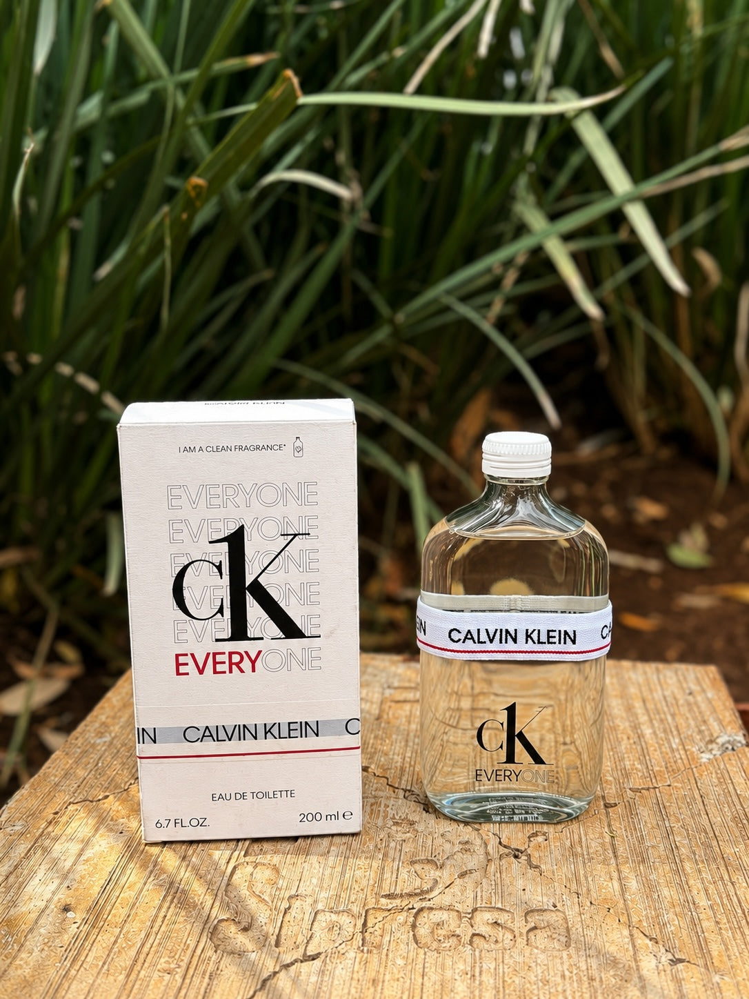 Perfume unisex 𝐋𝐔𝐀𝐋 CK Everyone de Calvin Klein con frasco de vidrio transparente y caja blanca en base de madera
