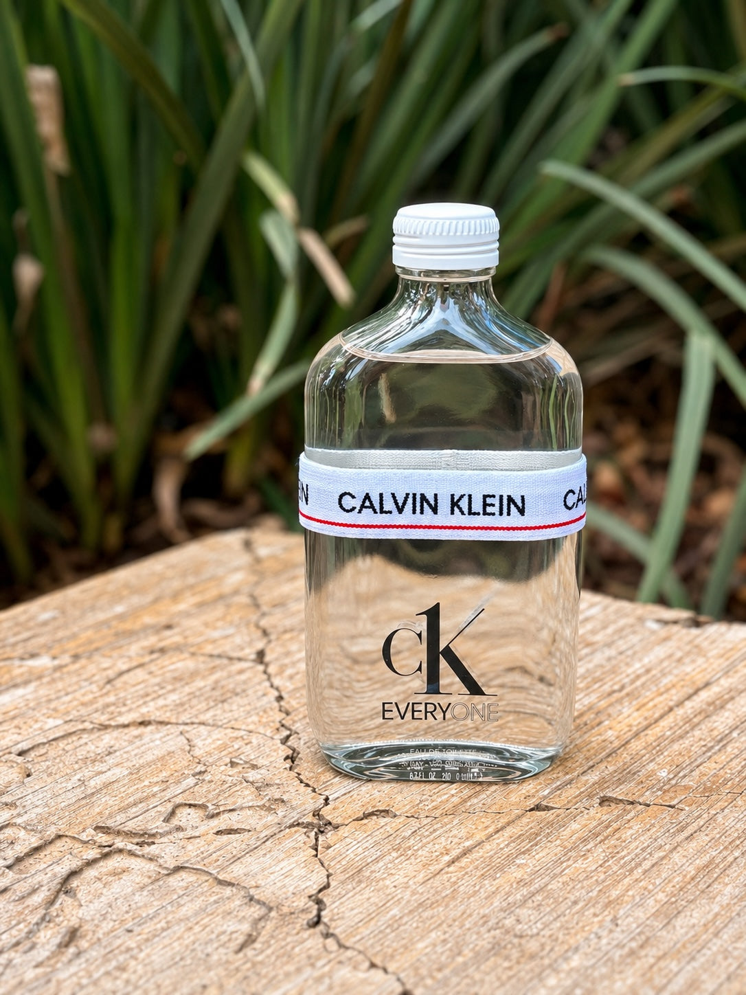 Perfume unisex 𝐋𝐔𝐀𝐋 Calvin Klein Everyone en frasco de vidrio transparente con banda elástica icónica en exterior.