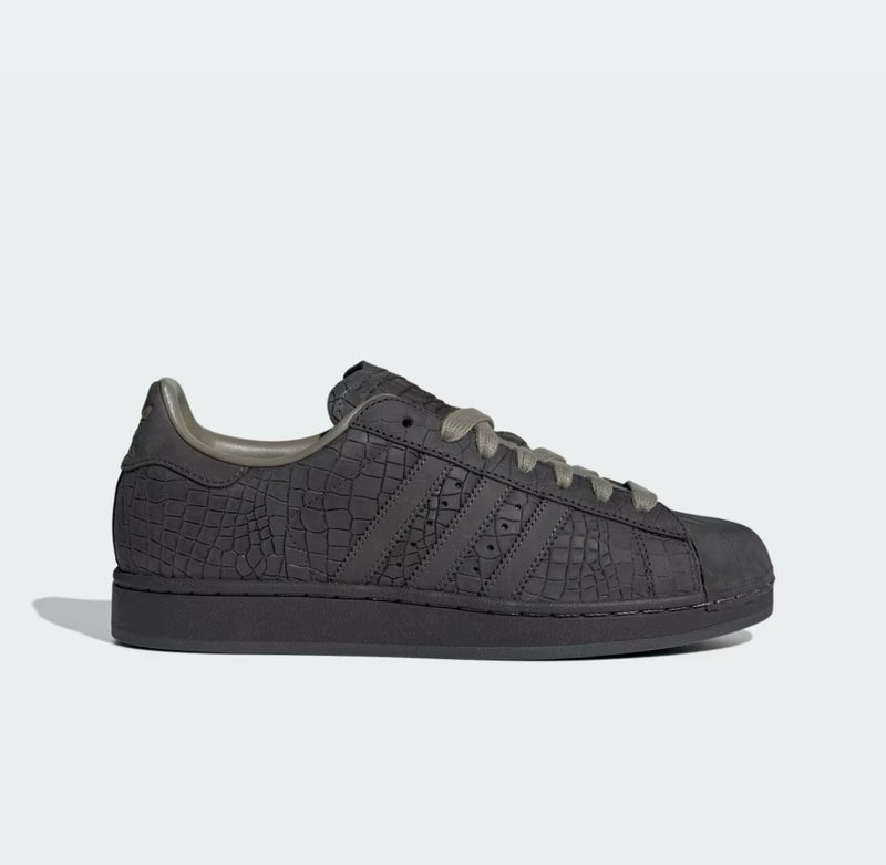 Tenis adidas Superstar 𝐋𝐔𝐀𝐋 en color gris oscuro con textura de piel de cocodrilo y punta de concha clásica.